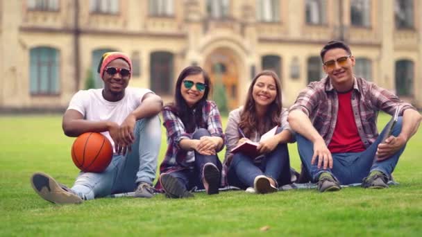 Multi estudiantes raciales se sientan en una hierba verde con pelota de baloncesto — Vídeo de stock
