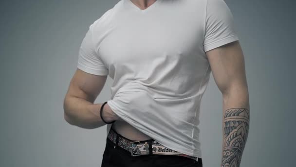 紧身衣 穿着牛仔裤的年轻人把一件白色T恤衫拉直 使其成为一种姿势 手臂交叉在胸前 与白色背景隔离 — 图库视频影像