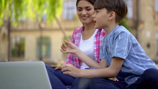 妈妈在大自然中和孩子们在一起 儿子用笔记本电脑在新鲜空气中训练 回答她的问题 女儿则坐得更近 — 图库视频影像
