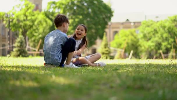 8岁的兄妹坐在公园的草地上 牵着彼此的手笑着等待父母的款待 — 图库视频影像