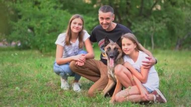 Belçikalı Malinois 'li bir aile çimenlerde oturuyor ve gülümsüyor.