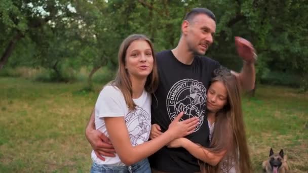 Отец обнимает и целует своих дочерей в парке — стоковое видео