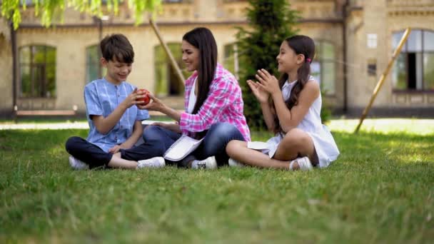 母親は子供と一緒に座って学校が隔離されている間 新鮮な果物を例にして新鮮な空気でレッスンを行うか 軽食のために持ち込まれたプロモーション — ストック動画