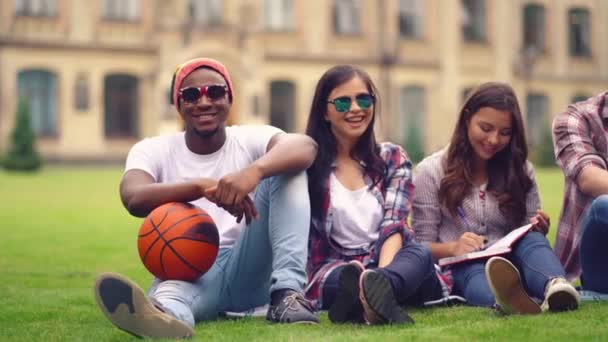 Друзья сидят на траве после баскетбольной тренировки — стоковое видео