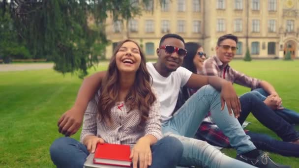 Skupina studentů se baví mezi vyučováními na trávníku u univerzity — Stock video