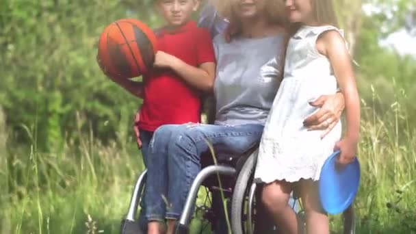 カメラのためにポーズを取る彼女の娘と息子を抱きしめる車椅子の母. — ストック動画