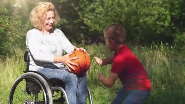 Son spelar kasta boll med mamma i en rullstol på en bakgård. — Stockvideo