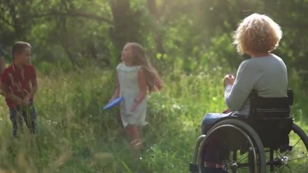 Çocuklar ve babaları tekerlekli sandalyede anneleriyle frizbi oynuyorlar.. — Stok video