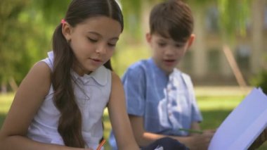 Kız ve erkek kardeşlerin defterleri dışarıda oturup ödevlerini yapıyorlar.