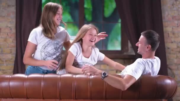 Две девочки-подростки играют со своим отцом на диване — стоковое видео
