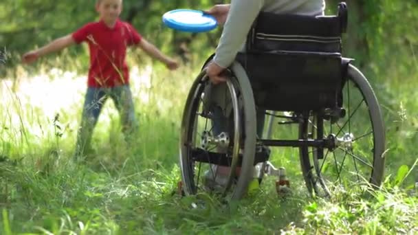 Matka na kolečkovém křesle hraje frisbee se synem venku. — Stock video