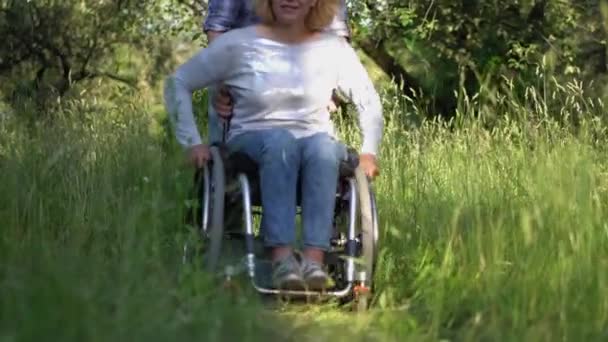 Vader helpen moeder in een rolstoel krijgen naar kinderen spelen in een weide — Stockvideo