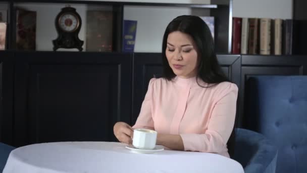 Mujer asiática sentada en una mesa en el restaurante y tomando un café — Vídeo de stock