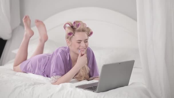 Egy fiatal lány laptoppal fekszik az ágyon.. — Stock videók