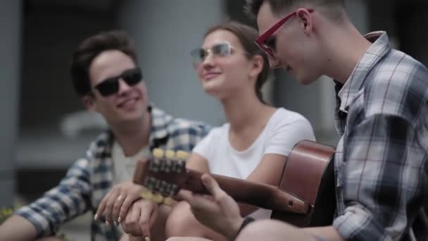 Young man playing on the guitar for friends sitting outdoors. — Stock Video