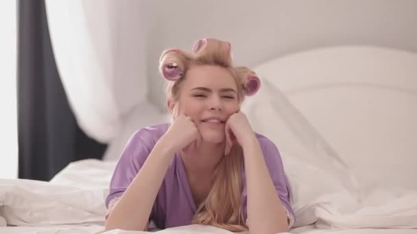 Uma mulher deitada feliz em uma cama com cabelo encaracolado . — Vídeo de Stock