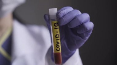 Üniformalı ve tek kullanımlık eldivenli bir mikrobiyolog. Halı etiketi 19 olan test tüpü. Bir hastanın kanıyla test tüpüne yakın çekim yap. Prores 422