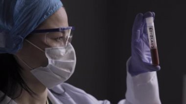 Mikrobiyolog doktor COVID 19 koronavirüsün kanına sahip bir test tüpünü alıyor, sallıyor ve dikkatlice inceliyor, aşı testlerine hazırlanıyor. Yakın plan. Prores 422
