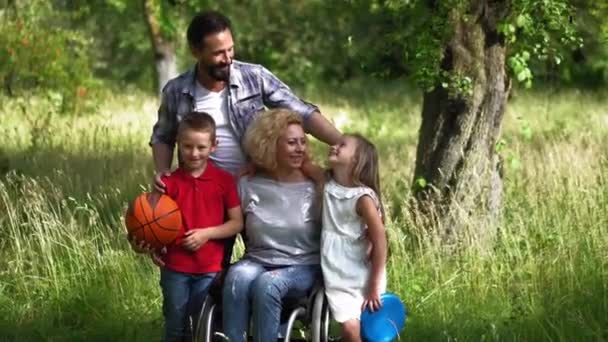 車椅子の母親と家族を愛することは、自然の中で家族の写真を撮る、子供たちは彼らの母親が頬に彼女にキスを抱きしめる。家族の肖像画の概念。第四百二十二条 — ストック動画