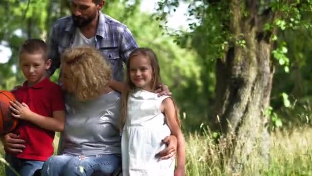 Οικογένεια με μια μητέρα σε αναπηρικό καροτσάκι να κάνει ένα οικογενειακό πορτραίτο να στέκεται στη φύση, παιδιά να αγκαλιάζουν τη μητέρα τους να τη φιλούν στο μάγουλο. Οικογενειακό πορτραίτο. Πρότυπα 422 — Αρχείο Βίντεο