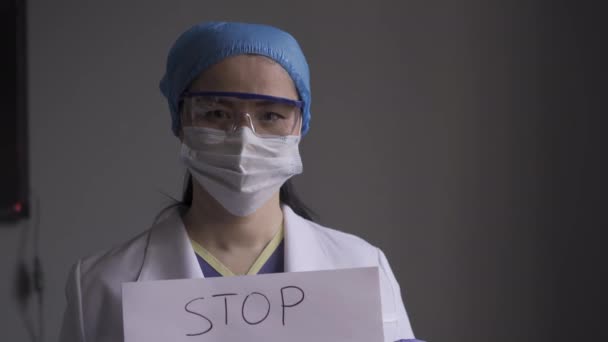 Врач в медицинской форме стоит в больничном кабинете и держит плакат с надписью STOP COVID 19. Врачи во время пандемии. Слайд камеры. Прорес 422 — стоковое видео