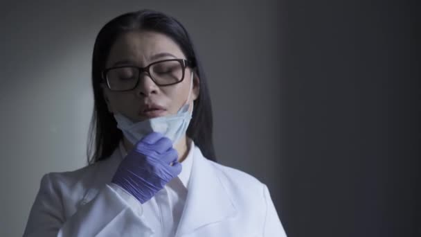 Лікар зітхає з полегшенням, видаляючи маску з обличчя. Жіночий лікар стомився під час пандемії коронавірусу. Проходить 422 — стокове відео