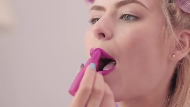 Blondine in quarantaine schildert haar lippen. Een jong meisje zit thuis tijdens de quarantaineperiode. Het coronavirus stopt haar lippen in lippenstift om zich beter te voelen. Sluit maar af. Prores 422 — Stockvideo