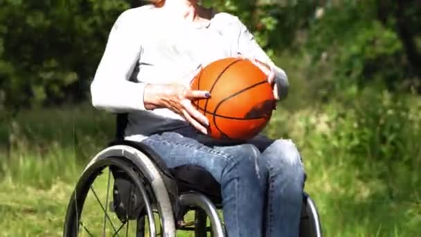 Una mujer en silla de ruedas al aire libre sostiene una pelota en sus manos, la lanza a sus hijos jugando fuera del marco. Concepto familiar. Prores 422 — Vídeo de stock