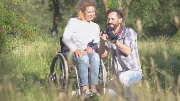 Une famille de deux personnes une femme en fauteuil roulant pose pour le mari d'un photographe dans la nature. Un couple au milieu de 30, 40 ans passe du temps ensemble dans le parc à faire des photos de famille. Prores 422 — Video
