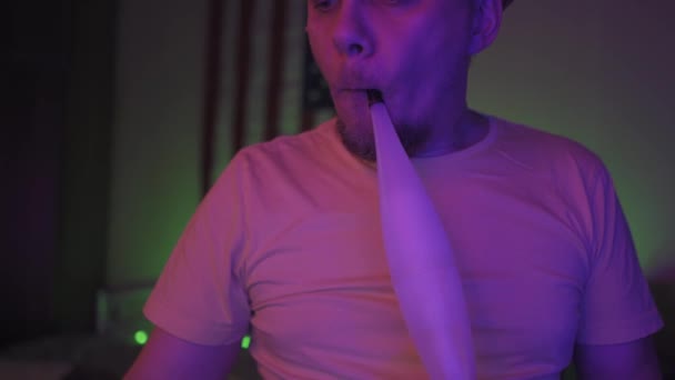 Um blogueiro rindo da câmera fuma um narguilé no ar de seu canal de mídia social. Um jovem relaxa sentado em uma sala com iluminação de néon e fumando um narguilé. Prores 422 — Vídeo de Stock