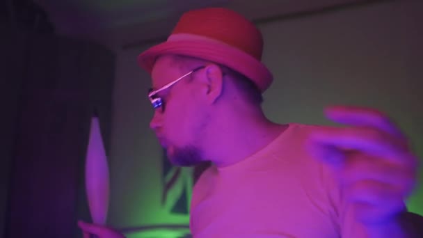 Man smokes, exhales smoke. Steam from an hookah. Handsome man dancing sitting in the dark semi lit neon light room wearing sunglasses with UK flag on the wall behind him. Prores 422 — Stock Video