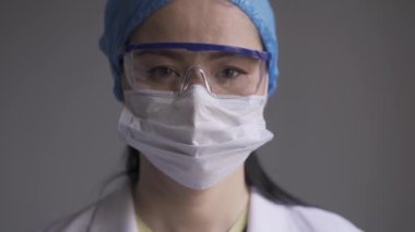 Koruyucu maskeli bir hemşire ya da doktor kameraya bakıyor. Yorgun gözlü Asyalı doktor hastaya bakıyor. Sağlık hizmeti konsepti. Kapatın. Prores 422