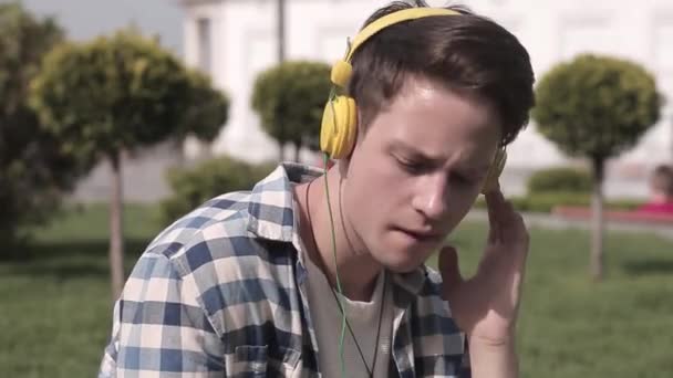 Estudiante Hipster escuchar música sentado al aire libre en el fondo de la ciudad. El joven escucha su canción favorita sentada en una hierba. Prores 422 — Vídeos de Stock
