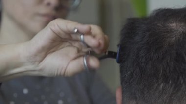 Kadın kuaför genç adamın saçını kesiyor. Bulanık saçlı bir kuaförü olan genç bir adamın kafasına yakın plan. Müşteri başkanına odaklan. Prores 422