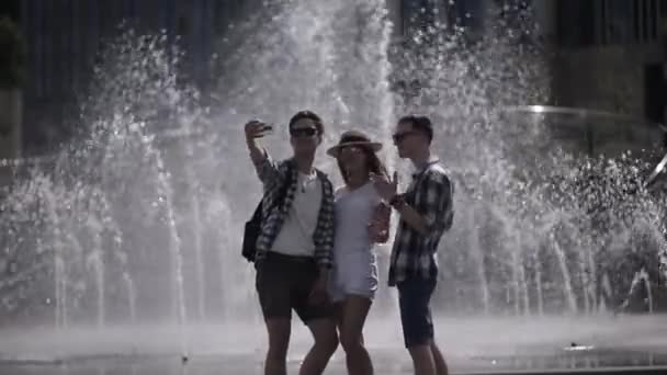 Przyjaciele robią sobie selfie przy fontannie w turystycznym miejscu, podróżując razem po kraju. Dwóch facetów i dziewczyna spędzają lato podróżując razem. Prores 422 — Wideo stockowe