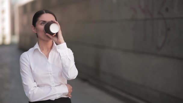 Zakenvrouw drinkt koffie uit een wegwerpbeker terwijl ze buiten naast het businesscentrum staat. Meisje in zakelijke kleren op de achtergrond van het kantoor. Bedrijfsconcept. Prores 422 — Stockvideo