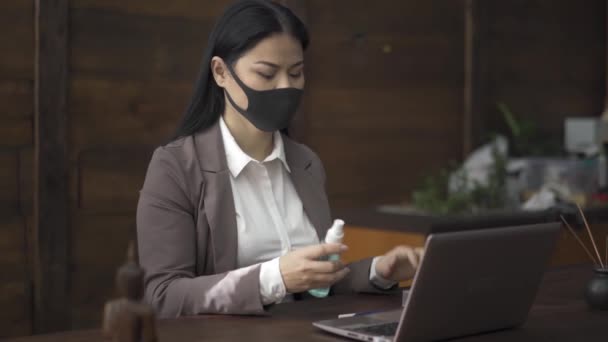 Mujer de negocios asiática en máscara protectora trabajando en el ordenador portátil y desinfectar sus manos con líquido que se encuentra a su lado. Gente de negocios trabajando durante los días de cuarentena del coronavirus — Vídeo de stock