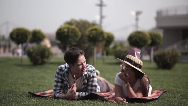 一对年轻夫妇躺在城市的草地上。在城市的草坪上，彼此相爱的青少年在聊天是很可爱的。友谊的概念。Prores 422 — 图库视频影像