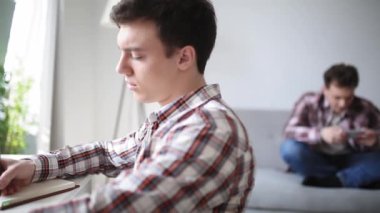 İki kardeş evde karantinada, biri akıllı telefonda oynuyor veya sosyal ağları izliyor, diğeri ise üniversitede oturup materyal okuyor. Evde kal konsepti. Prores 422