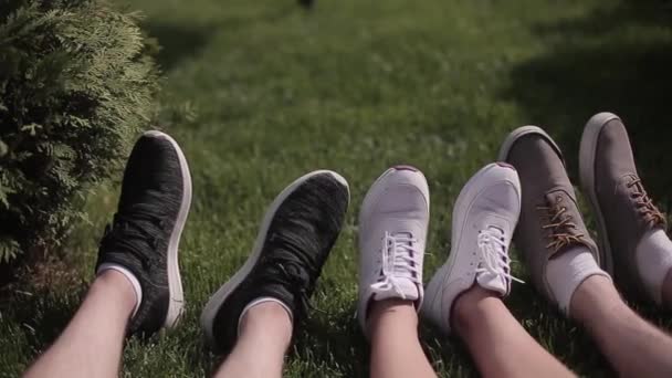 Primer plano en los pies de tres jóvenes hombres y niñas cansados sentados en la hierba verde en la zona de paseo de la ciudad. Concepto de viaje. Prores 422 — Vídeos de Stock