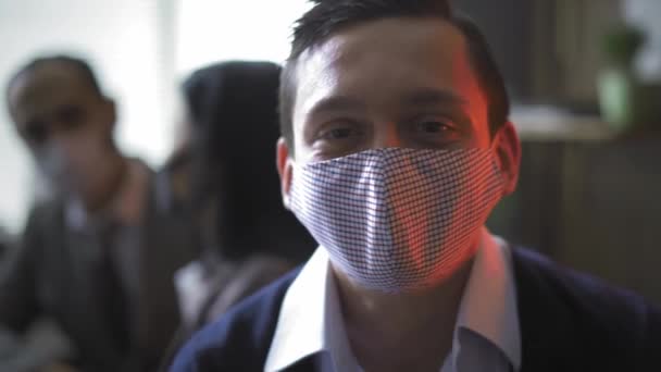 Young freelancer take of protective mask and make a funny face while works in the office with colleagues sitting in the background. Work during coronavirus pandemic concept. Prores 422 — Stock Video