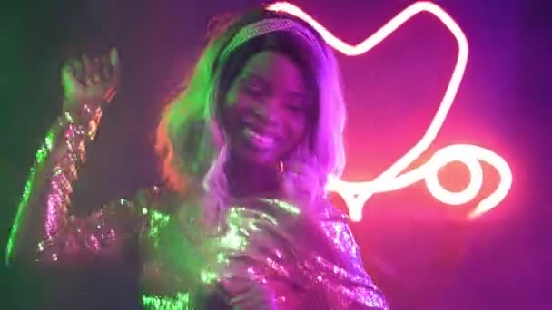 Egy afro-amerikai nő táncol egy sötét szobában neon fényekkel. szőke hajú lány táncol egy klubban, élvezi a zenét. Neon koncepció. Gyümölcsfélék — Stock videók