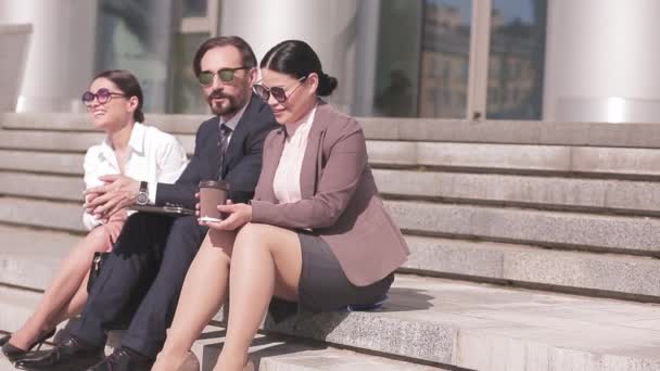 Geschäftsleute sitzen auf den Stufen vor dem Bürogebäude. Ein Mann und zwei Frauen in Businesskleidung bei einer Kaffeepause. Geschäftskonzept. Prores 422 — Stockvideo