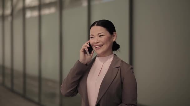 Aziatische zakenvrouw praten aan de telefoon het dragen van business suit staan buiten met een business office center op de achtergrond. Bedrijfsconcept. Prores 422 — Stockvideo