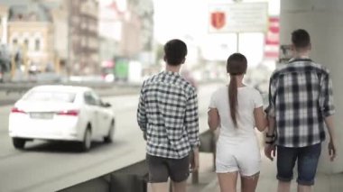 Yabancı bir şehirde seyahat eden gençlerin arka görüntüsü. Gençler, şehirde dolaşan iki erkek ve bir kız bir partiye ya da konsere giderler. Arkadaş kavramı. Prores 422