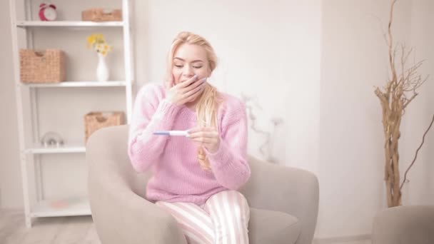임신 테스트를 받은 금발 소녀가 안락의자에 앉아 집에 앉아 있는 결과를 알게되어 기뻐 한다. 기대되는 아이의 행복 한 순간이다. 행복 한 가족 개념. 프로방스 422 — 비디오