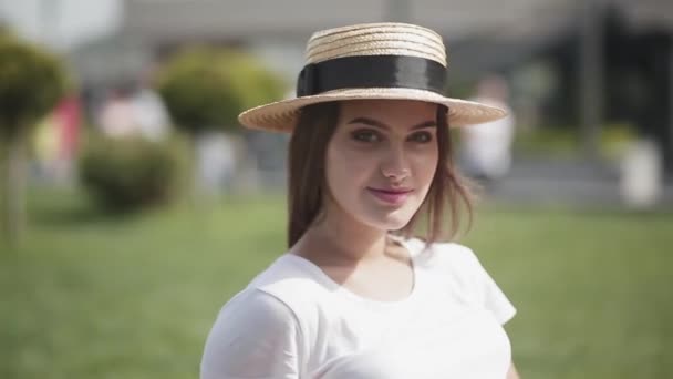 Menina olhando para a câmera em um chapéu vintage e sorrindo bonito timidamente. Uma menina aguarda um cara ou amigos em pé no fundo de uma cidade industrial. Prores 422 — Vídeo de Stock