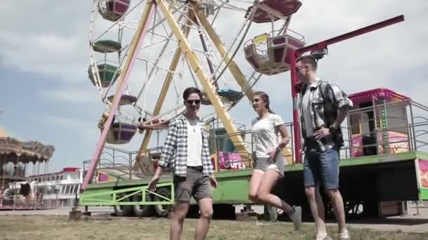 Amigos saltando alegremente na frente Ferris Wheel no fundo e uma cidade de carnaval visitante. Amigos a divertirem-se na baixa. Conceito de amigos. Prores 422 — Vídeo de Stock