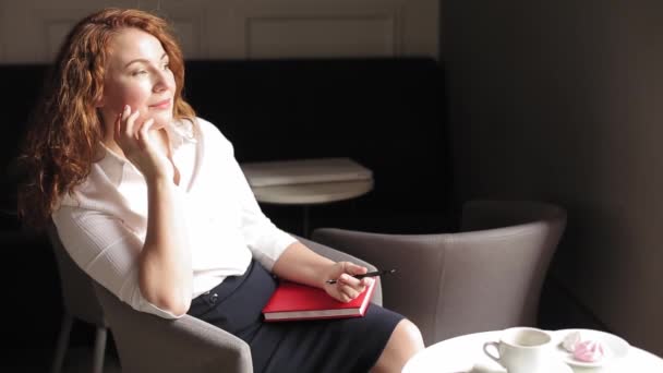 Business woman sits in a chair with a diary or a glider and makes notes and drinks coffee. A beautiful businesswoman is planning a week parsing meeting records. Prores 422 — Stock Video