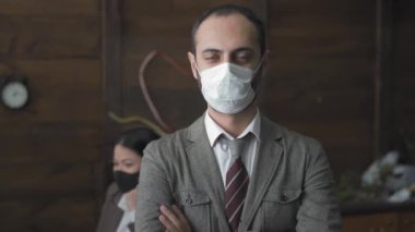 Koruyucu maskeli serbest çalışan bir adam kollarını kavuşturup kameraya bakıyor. Karantina sırasında ofiste çalışan yakışıklı bir serbest çalışan var. Prores 422